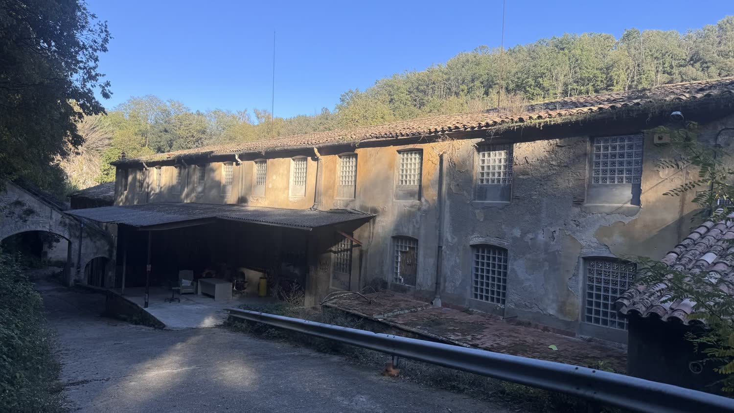 The 1886 factory building, stone and render, backed by wooded hillside