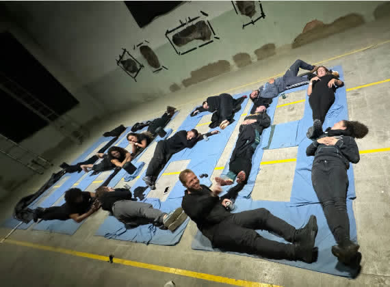 A group of people lying on blue mats on the factory floor during a performance